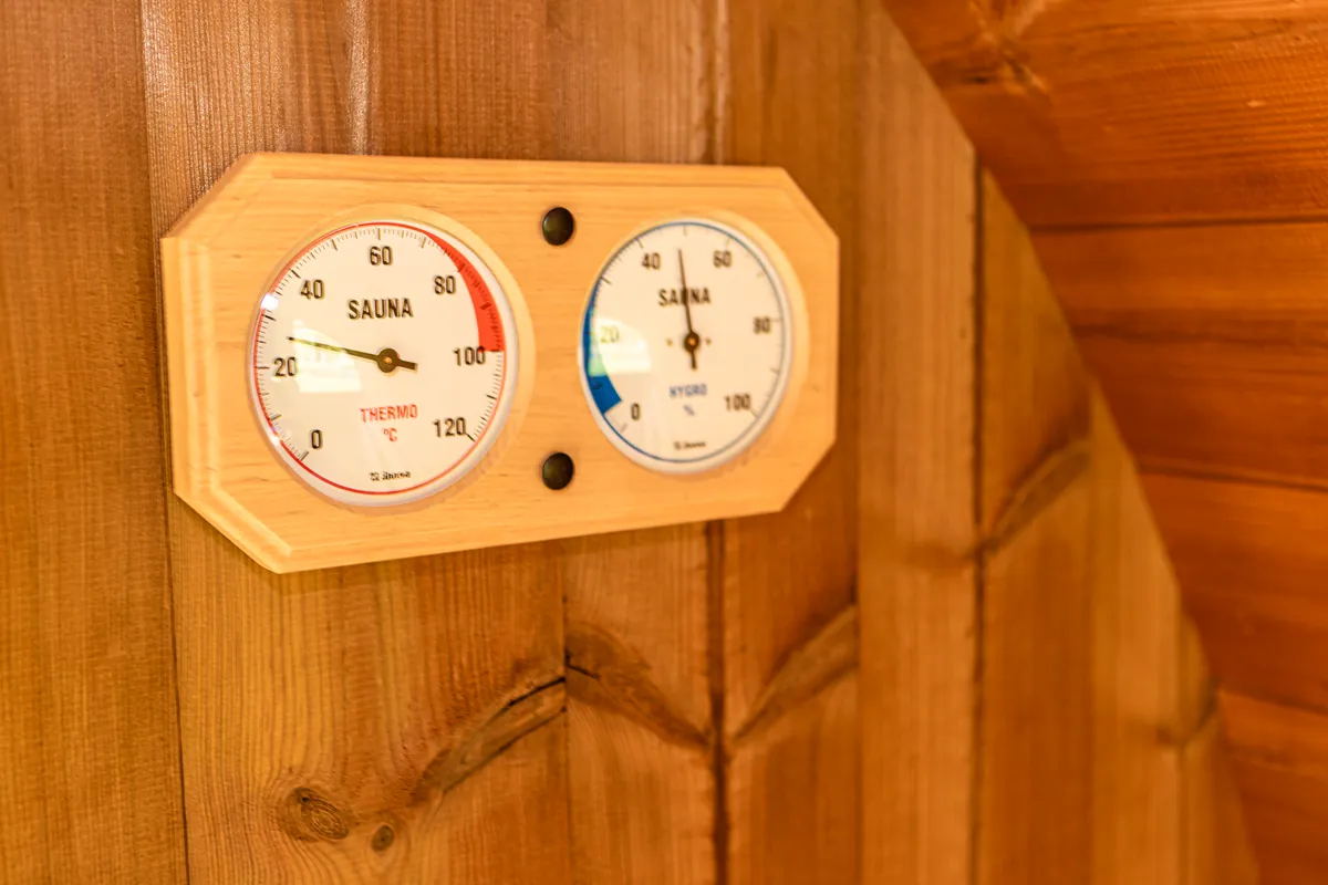 Thermometer und Hygrometer in einem Holzrahmen an der Saunawand.